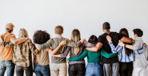 View from behind of a group of people standing side by side with their arms around one another. What's the point of recovery groups?