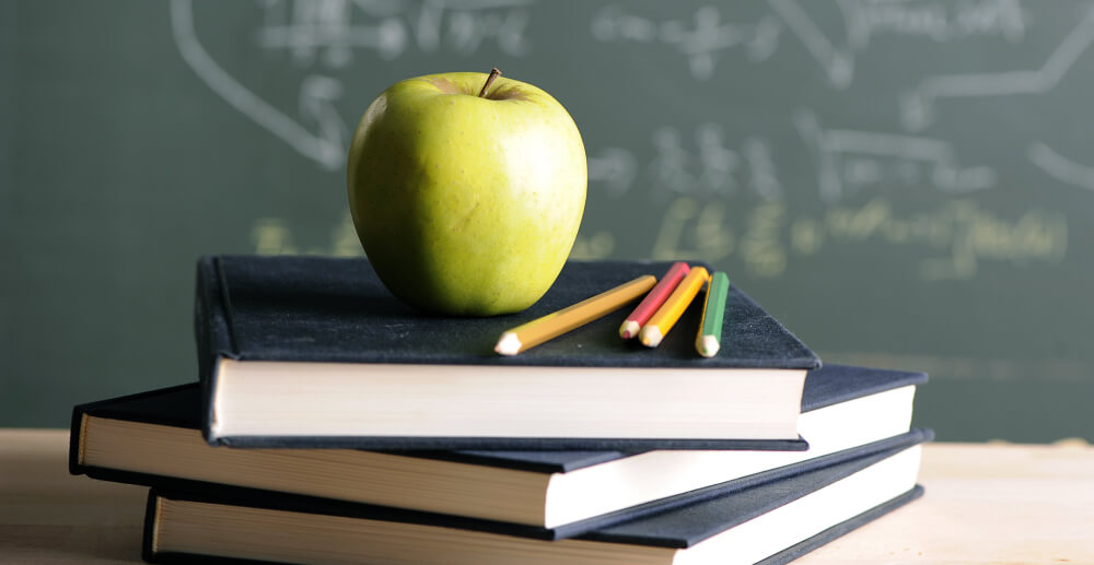 Green apple atop a stack of books on a desk. Addiction among teachers