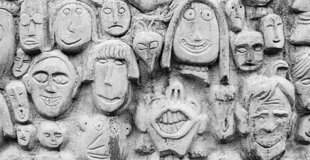 Bas relief of an eclectic mix of minimally detailed faces sculpted into a concrete wall. My recovery doesn't look like yours.