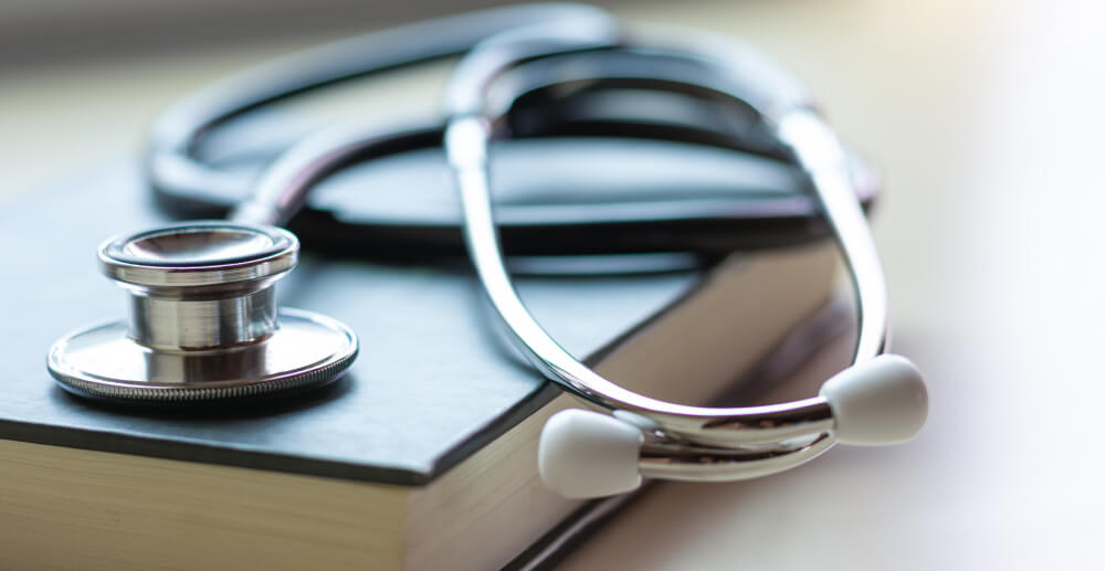 A closed book with a stethoscope coiled up on the cover.