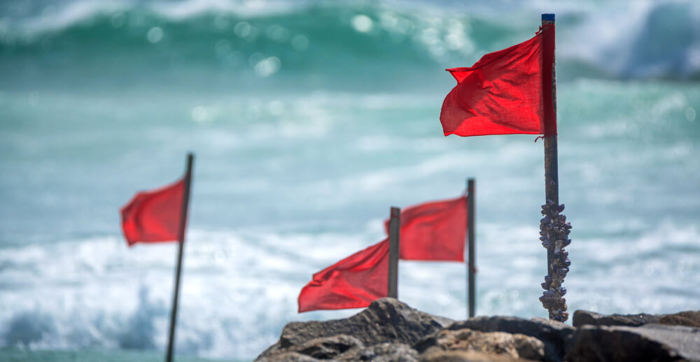 Four red flags planted on the beach and blowing in the wind.