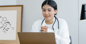 A young female doctor sits at a desk and speaks to a patient via a video conference.