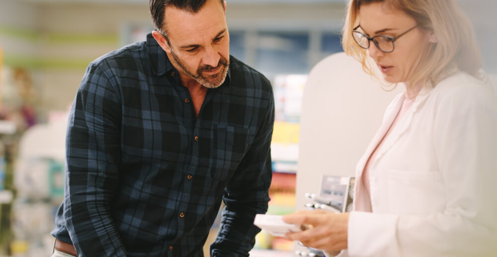 Middle-aged man leans forward as a female pharmacist explains a medication.