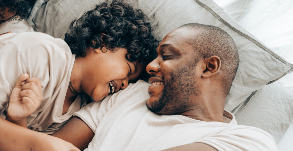 A Black father tickles his son, who laughs against his shoulder.