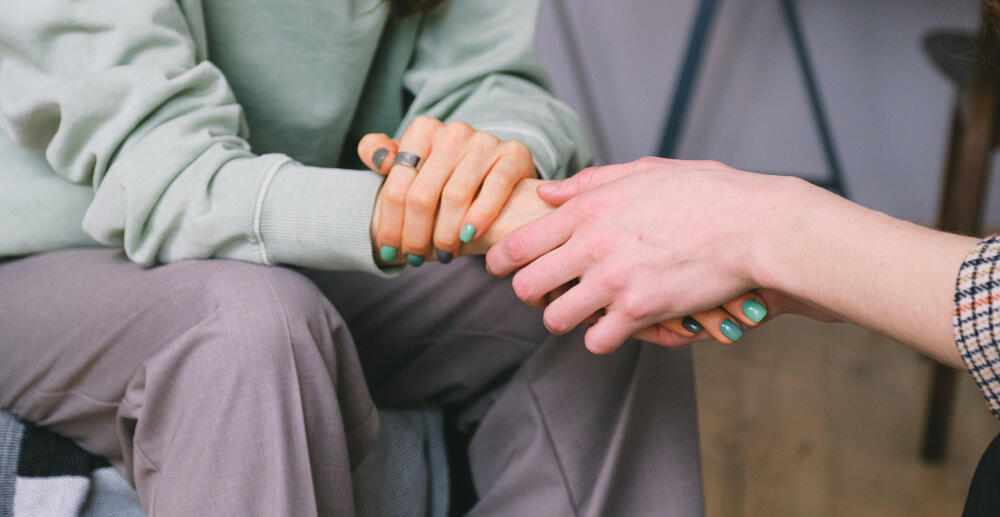 Closeup on the clasped hands of two people sitting closely together, facing one another.