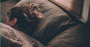 Woman sleeping on dark sheets, under a blanket.