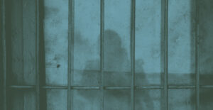 A concrete wall with metal bars in front of it, giving the impression of jail. The shadow of a woman falls across the bars and wall