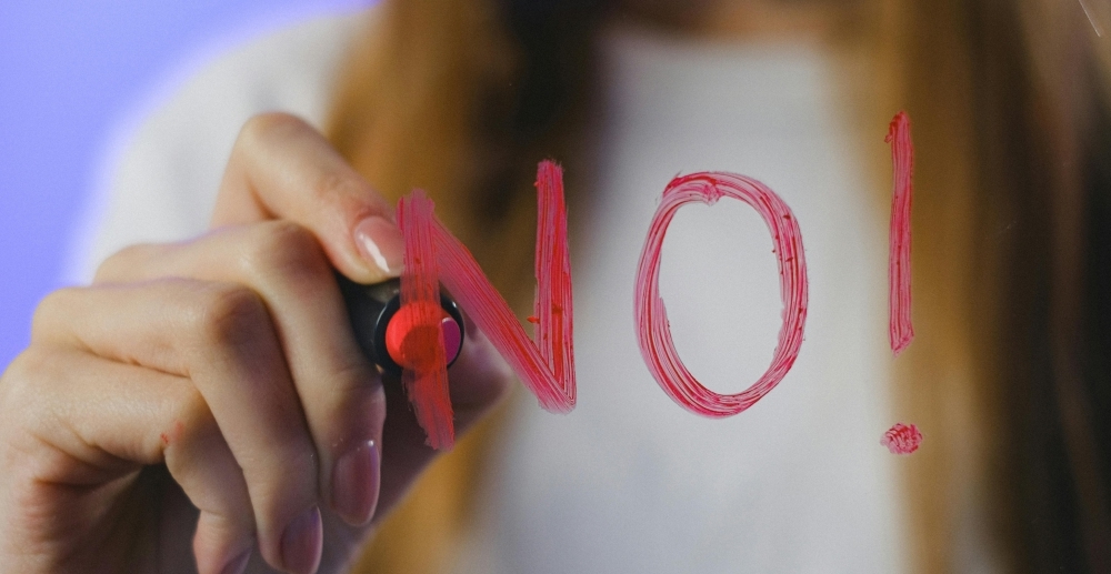 A woman writes the word "No!" on a clear surface in red lipstick.