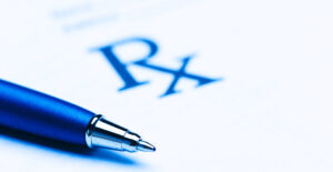 The Rx on a prescription pad is large but slightly out of focus. There is a pen resting on the prescrition pad