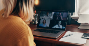 A woman sits at an open laptop, joining a video conference.