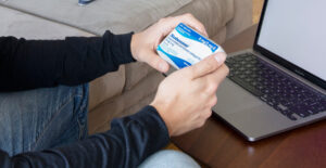 A man wearing a long-sleeved shirt and jeans looks at the Suboxone box held in his hands. He sits in front of an open laptop. Suboxone is sober.