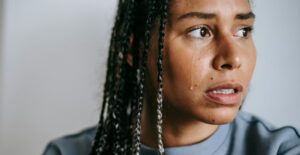 A woman with braids in her hair looks off-camera with a frightened expression, a tear running down her face