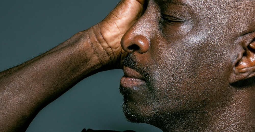 Profile view of a Black man with his hand up to his head in pain.