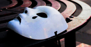 A white plastic tragedy mask discarded on a curved metal bench.