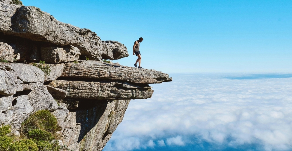 Seen from a distance, a man walks to the edge of a jutting, rocky cliff.