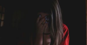 A woman sits in a dark room with her hands over her face.