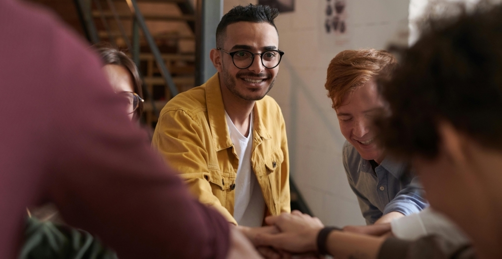A group of friends laugh and put their hands together in solidarity
