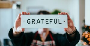 A person in an apron holds up a sign that says GRATEFUL over their face.