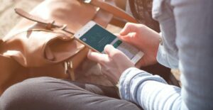 A person sits cross-legged outdoors, looking at the Monthly Health Check in their Workit Health app on a smartphone