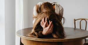 A woman slumps over a table with her head in her hands.
