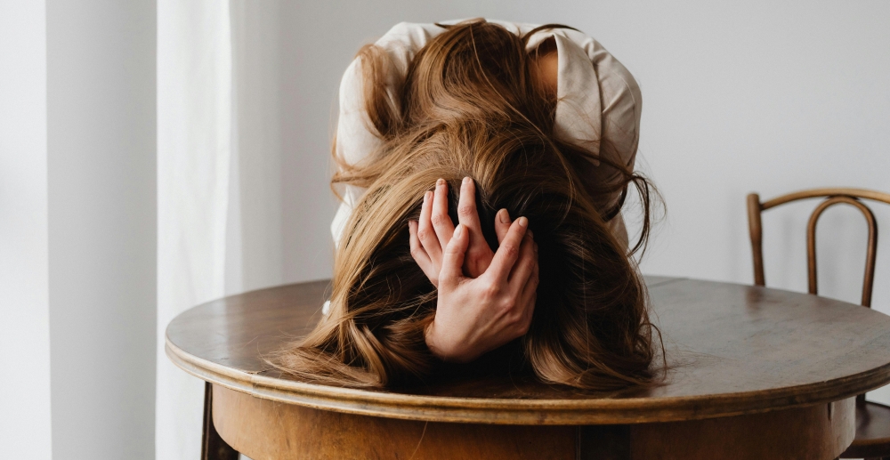A woman slumps over a table with her head in her hands.