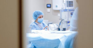 View through the window of a door at surgical prep, with a masked doctor