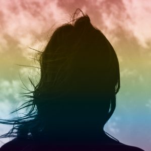 Silhouette of a woman's head against a sky that has a rainbow overlay. Coming out and coming clean.