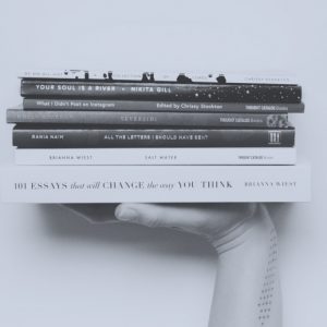 Light gray-blue color overlaying a black and white photo of a hand lifting a stack of books. Books to read in early recovery