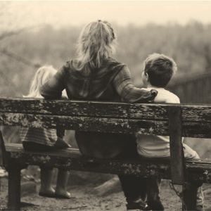 View from behind of a woman on a wooden bench with a child on either side of her. Confessions of an alcoholic mom, part 2