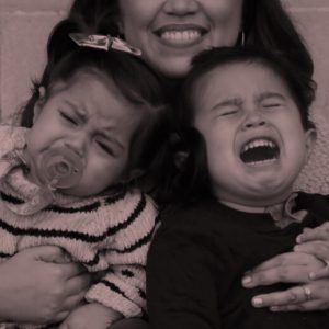 Woman holding two screaming toddlers. Confessions of an alcoholic mom