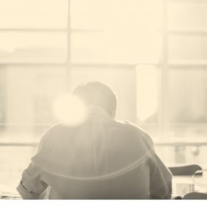 Man in an office, with a glare of light obscuring his outline. Opioid addiction at work.