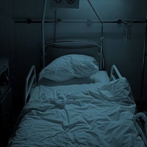 An empty hospital bed with rumpled sheets, with a dark blue color overlay on the photo. Staying sober through a parent's death.