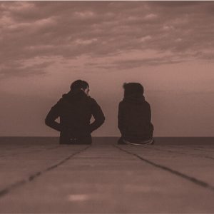 View from behind of two people sitting on the end or a pier, talking. Stay sober through a breakup