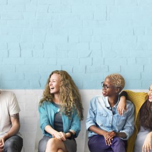 A row of people sit against a cinderblock wall, smiling and laughing together.