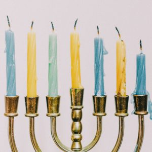 A brass menorah with seven blue and yellow candles. The candles are unlit but have darkened wicks and melted wax to show that they've been lit before.