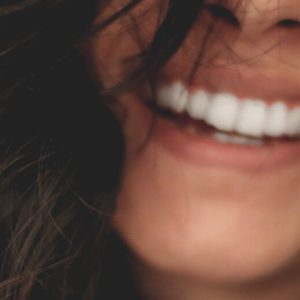 Close-up of a woman's smiling mouth. Her teeth are straight and white, and her long brown hair falls loose around her face.