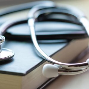 A closed book with a stethoscope coiled up on the cover.