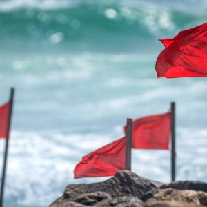 Four red flags planted on the beach and blowing in the wind.