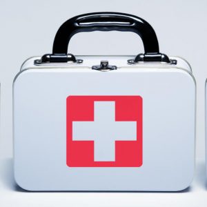 Three white, metal First Aid kits with red cross logos on the front of them. The background is a white counter against a white wall.