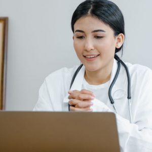 A young female doctor sits at a desk and speaks to a patient via a video conference.