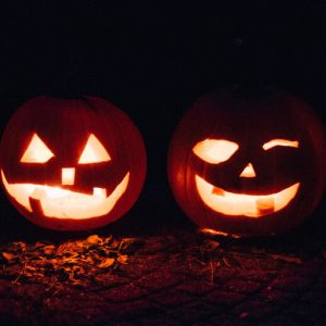 Light glows through the carved faces of a pair of jack o'lanterns sitting on a dimly lit ground.
