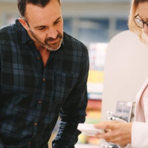 Middle-aged man leans forward as a female pharmacist explains a medication.