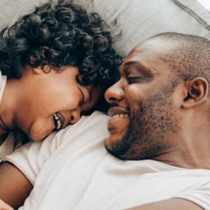 A Black father tickles his son, who laughs against his shoulder.