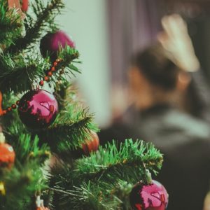 A decorated Christmas tree is in the foreground, and people are out of focus in the background.