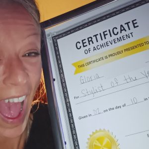 Gloria smiles wide, holding up a certificate of achievement