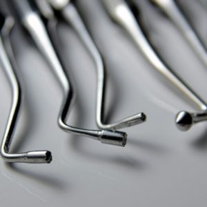 A row of metal dental picks and probes on a whiny white surface.