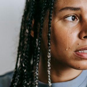 A woman with braids in her hair looks off-camera with a frightened expression, a tear running down her face