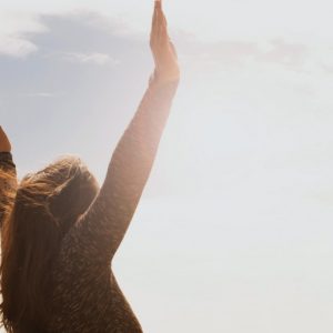 A woman with her hands flung into the air in celebration, silhouetted against the bright sky.