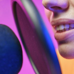 Closeup on a woman's mouth as she speaks into a microphone shielded by a pop filter