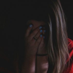 A woman sits in a dark room with her hands over her face.